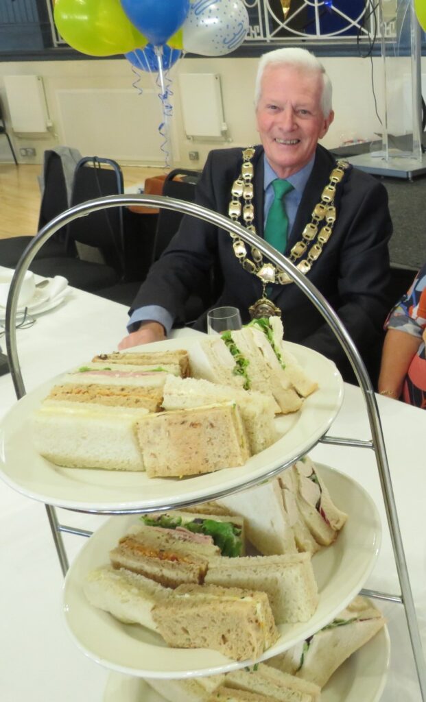 picture of the Mayor, John Crockford-Hawley sitting behind some cakes